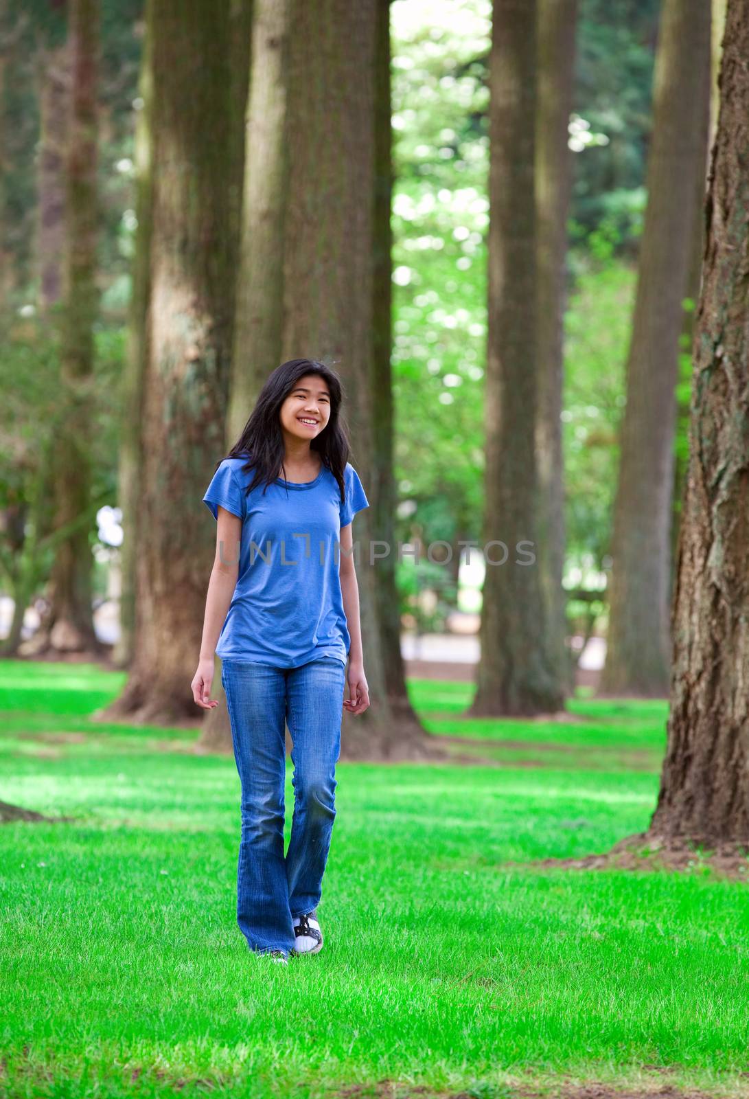 Young teen biracial girl walking under tall trees by jarenwicklund