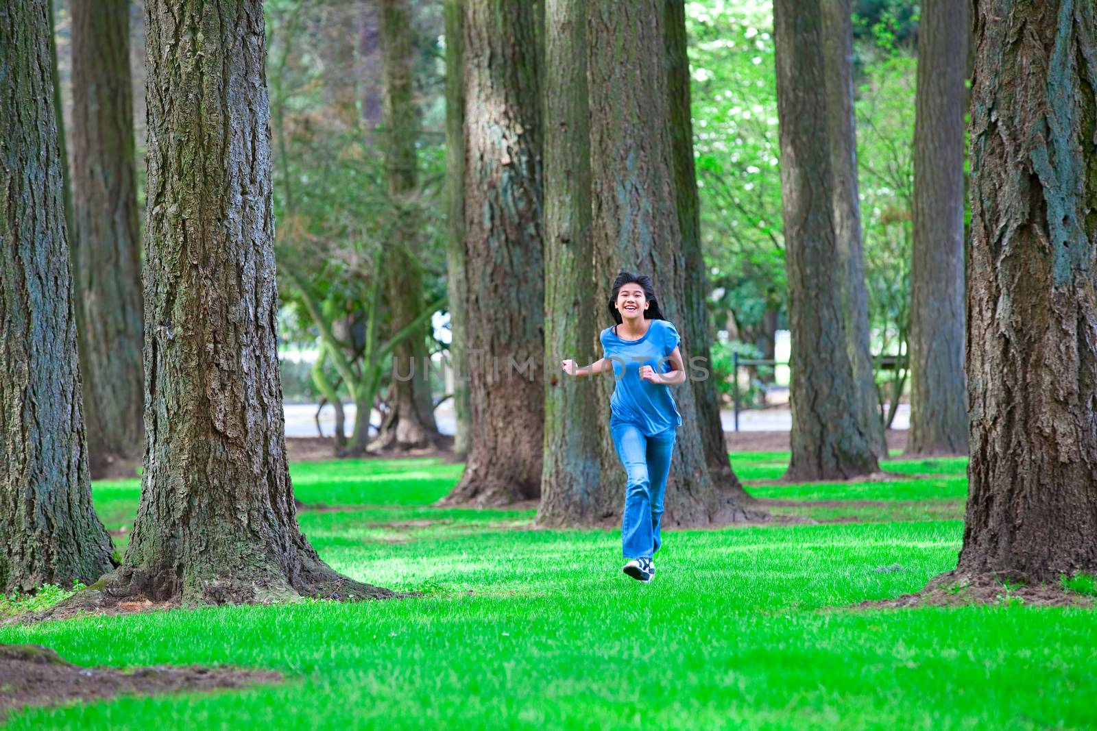 Young teen biracial girl walking under tall trees by jarenwicklund