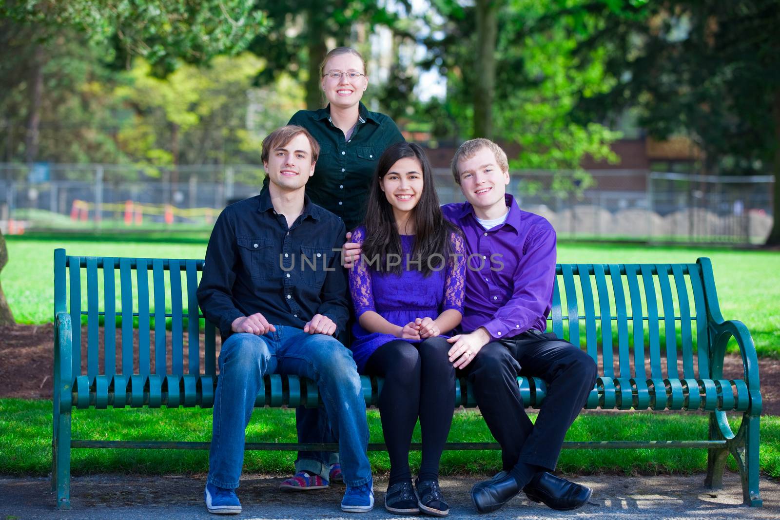 Four young multiethnic friends in early twenties  together sitting  at park