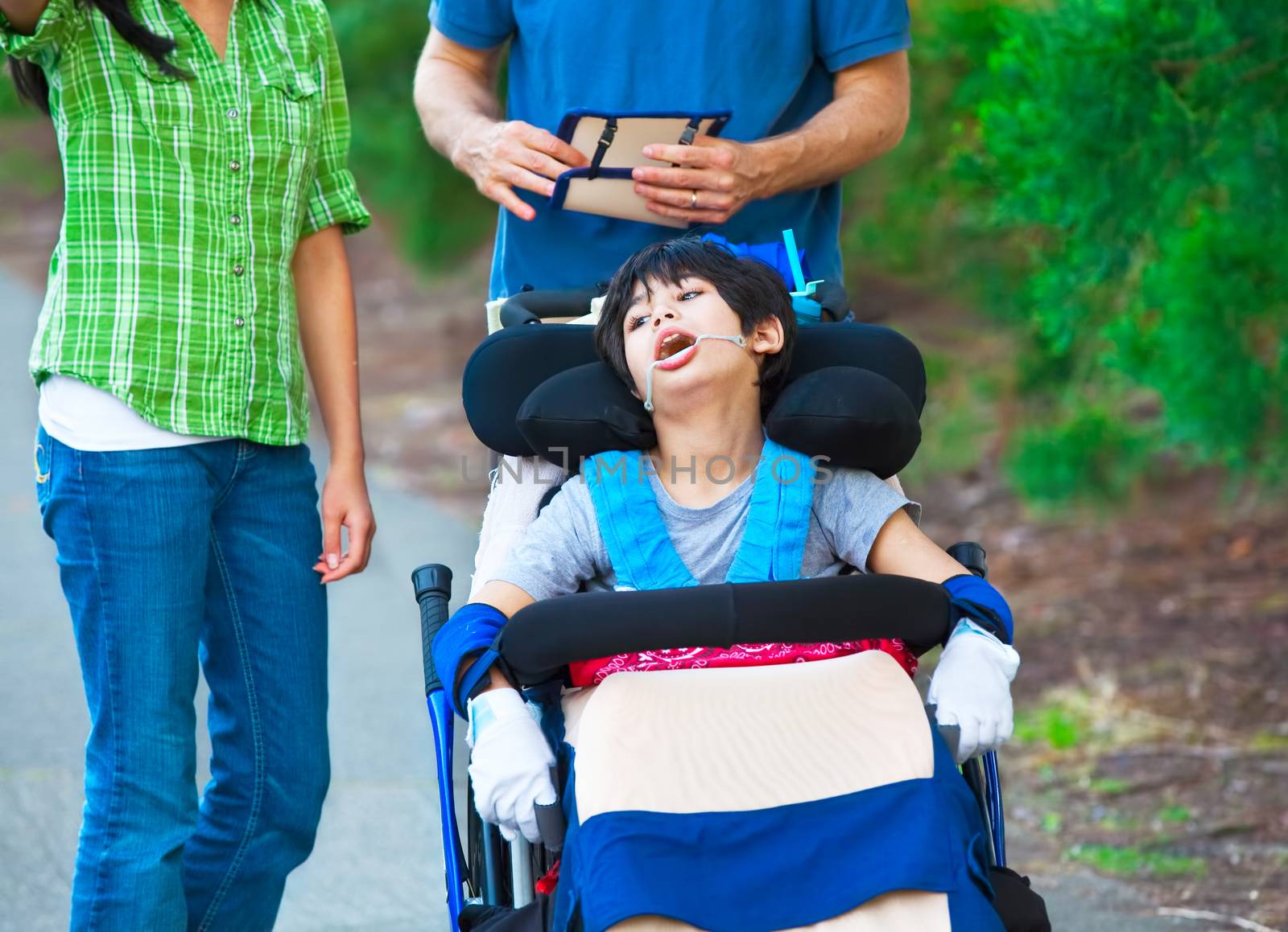 Disabled child in wheelchair outdoors with caregivers or family. Cerebral palsy.