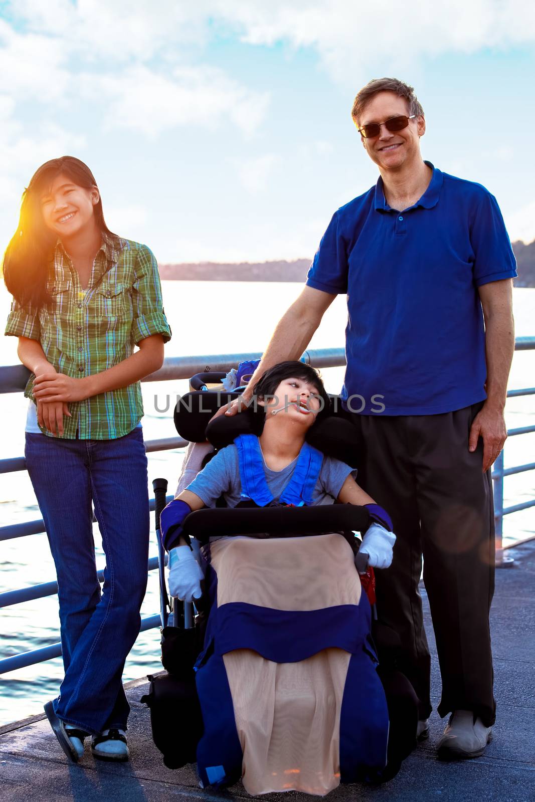 Disabled biracial child in wheelchair outdoors by lake with family. he has cerebral palsy.