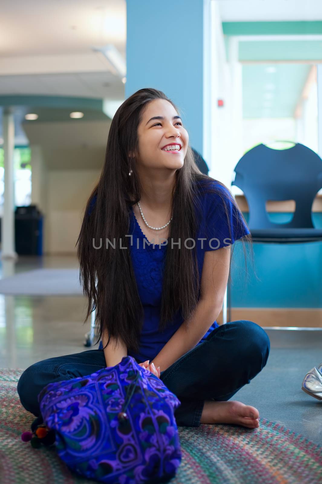 Beautiful biracial teen girl sitting crossed legged on floor smiling, looking up to the side