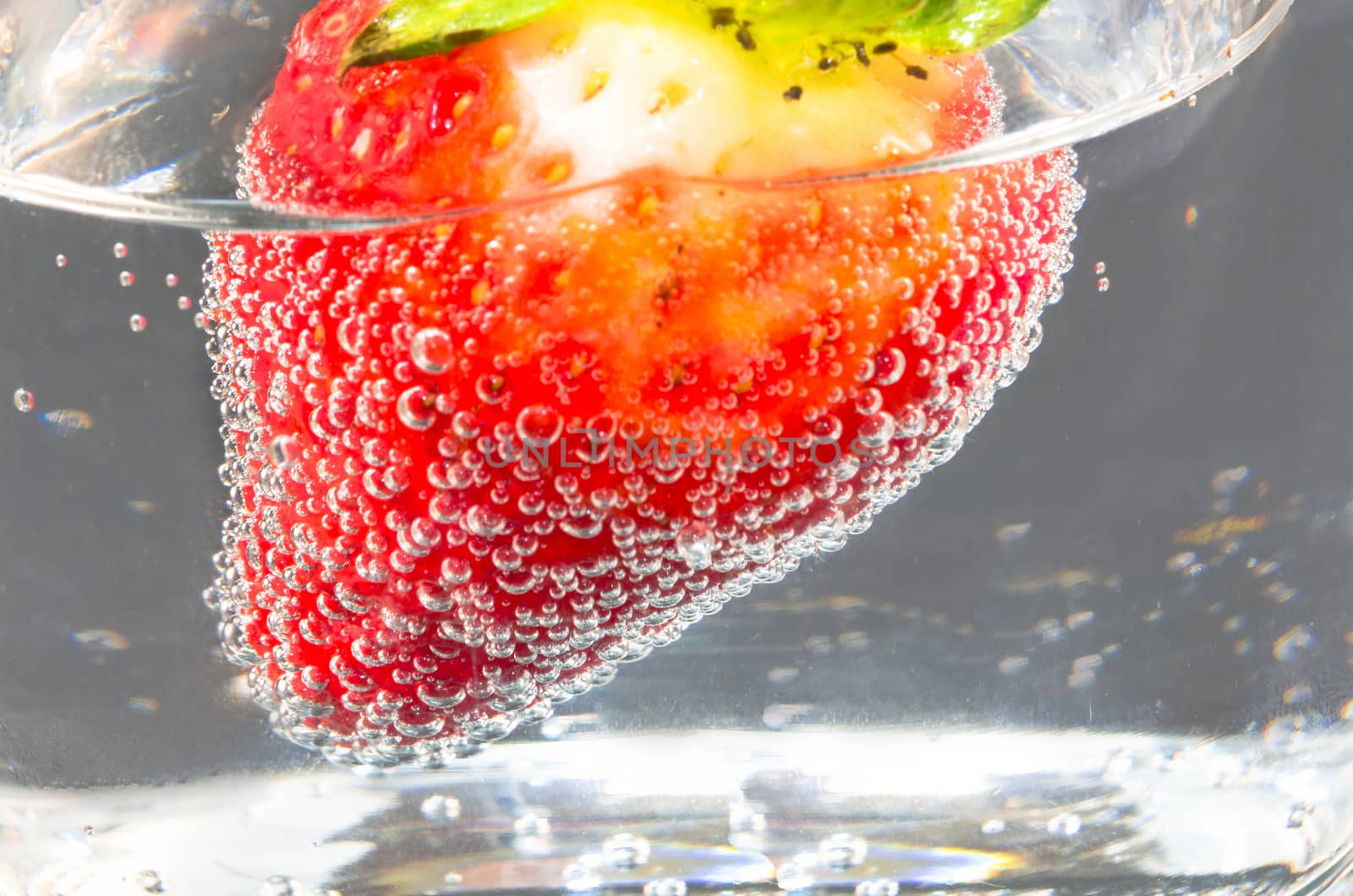 Close-up of strawberry floating in sparkling mineral water glass.

