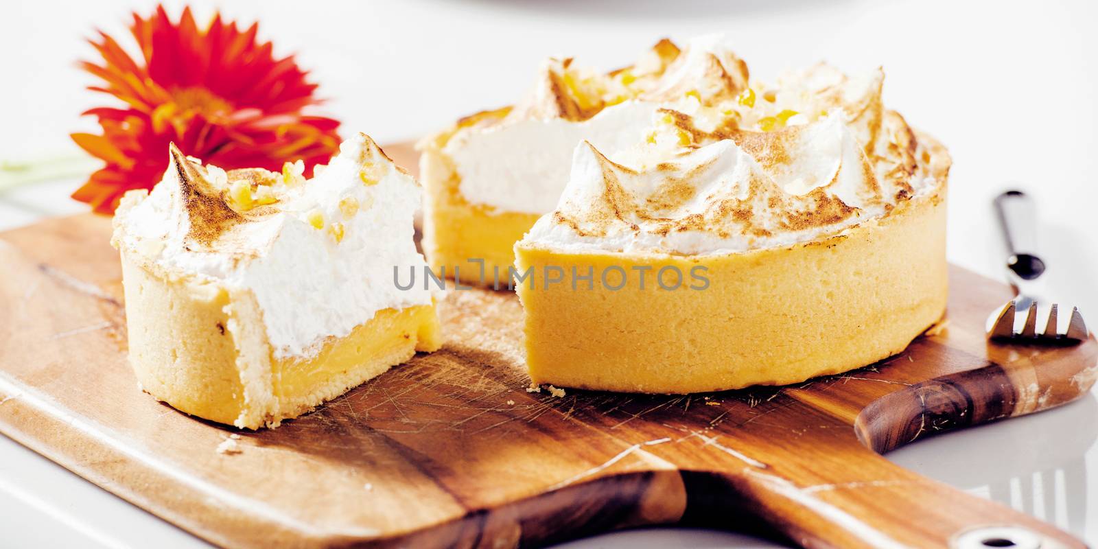 Lemon meringue pie on a timber board with a flower and plate in the background