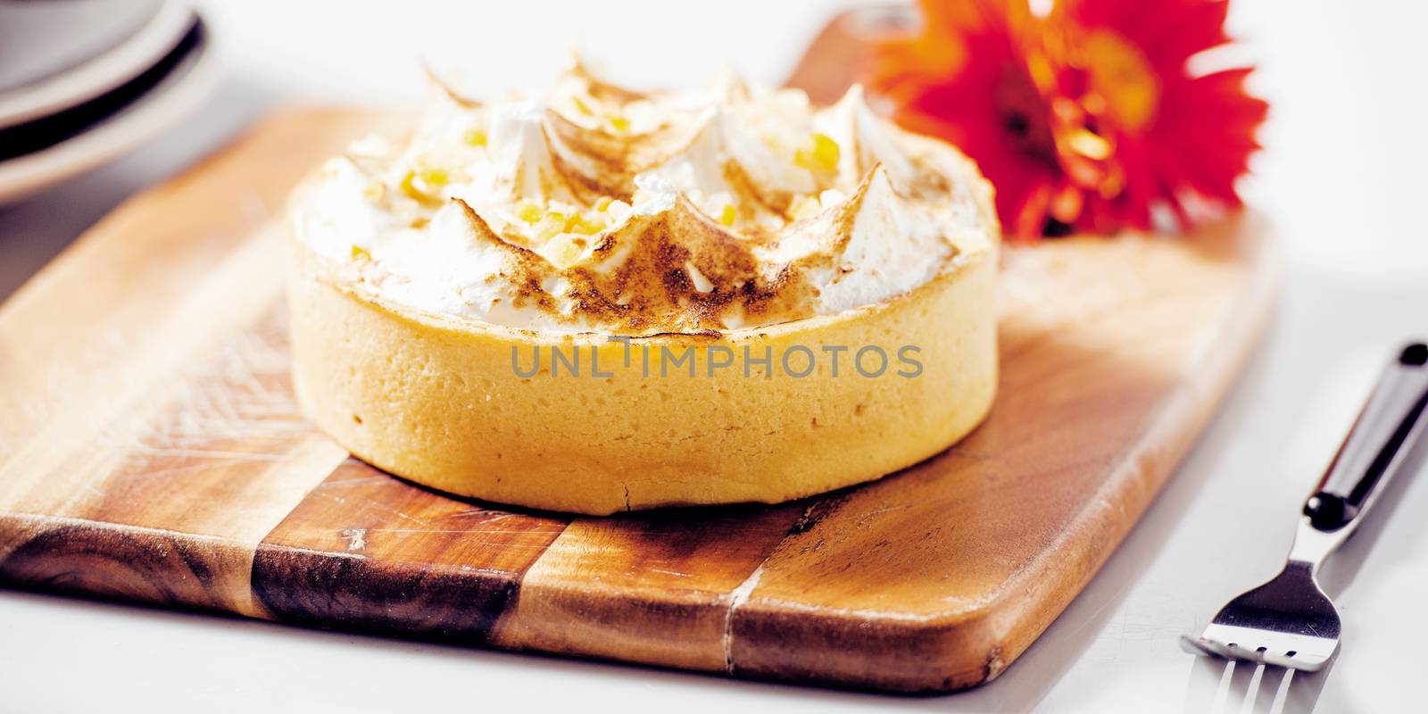 Lemon meringue pie on a timber board with a flower and plate in the background