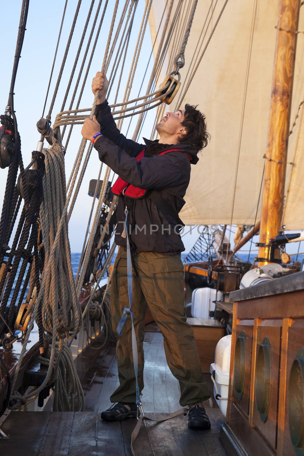 Young sailor on a ship's deck hoisting a sail