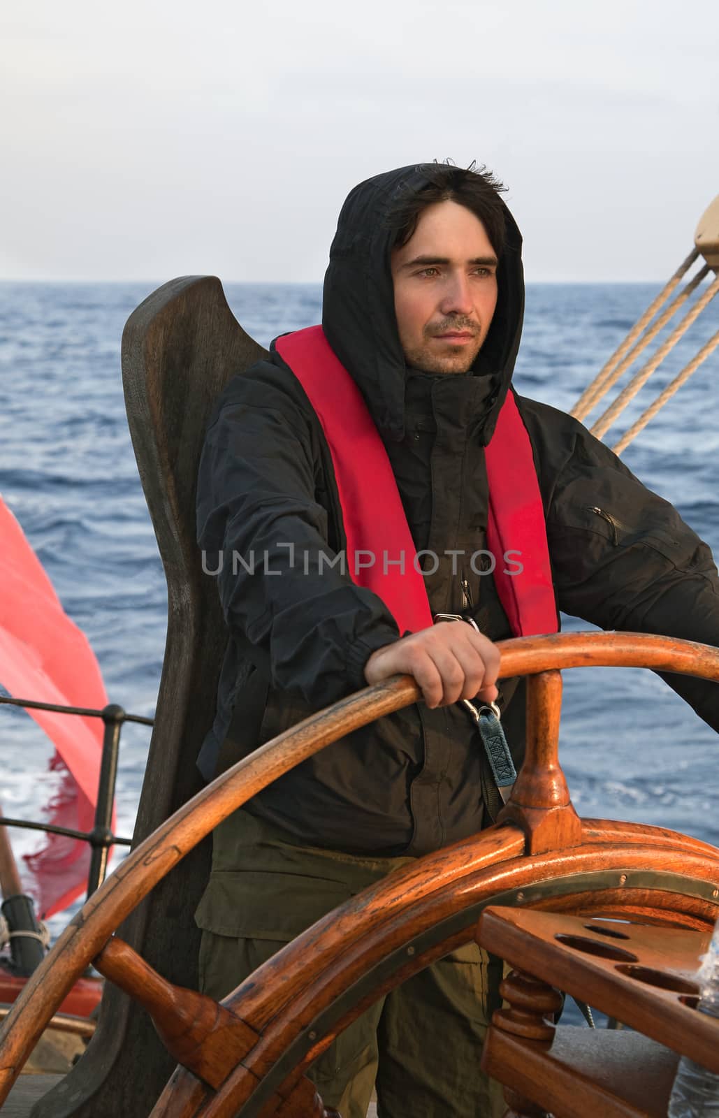 Young sailor on a ship's deck behind a steering wheel