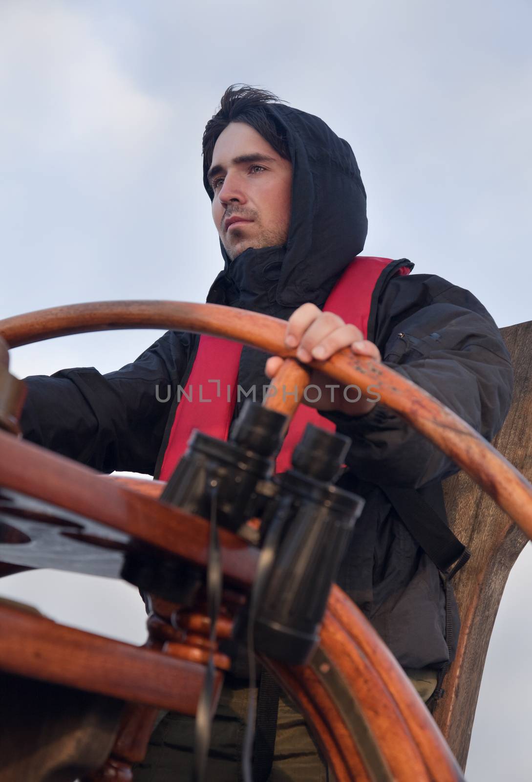 Young sailor on a ship's deck behind a steering wheel