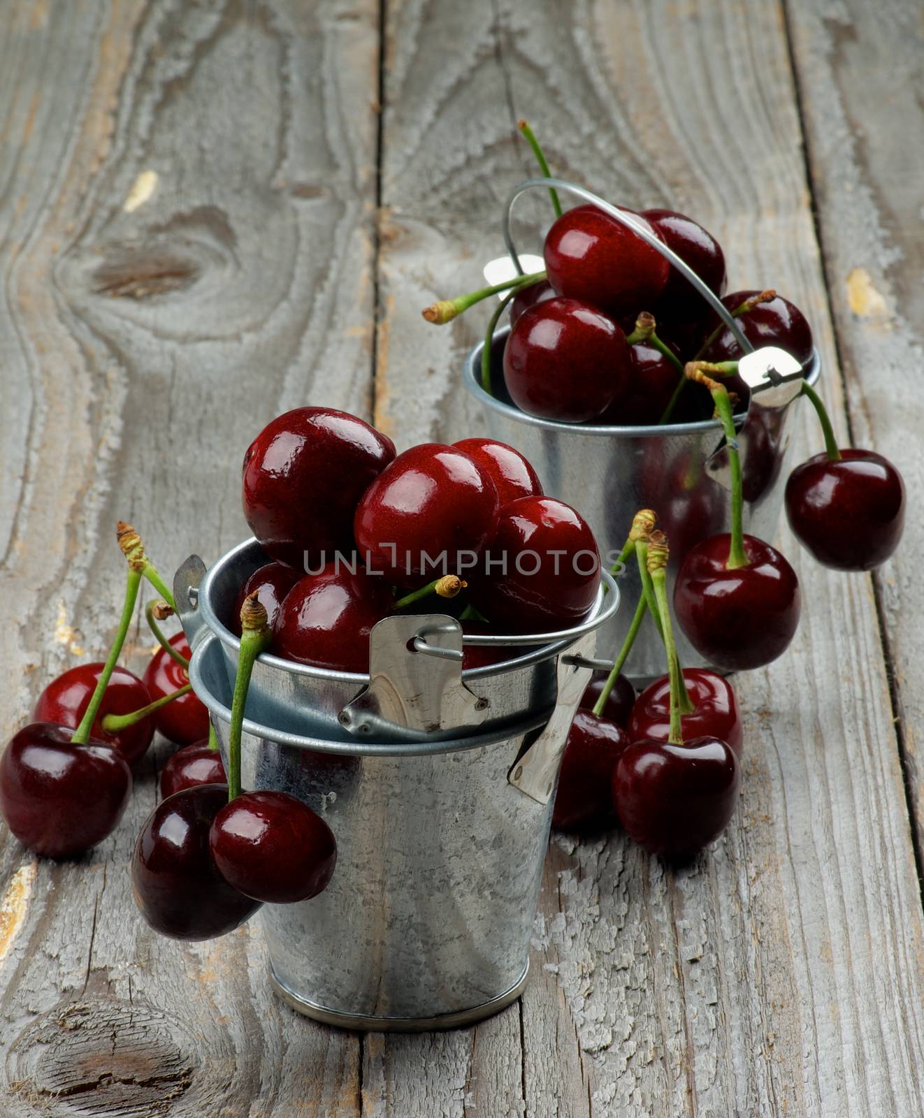 Sweet Dark Red Cherries in Two Tin Buckets closeup on Rustic Wooden background