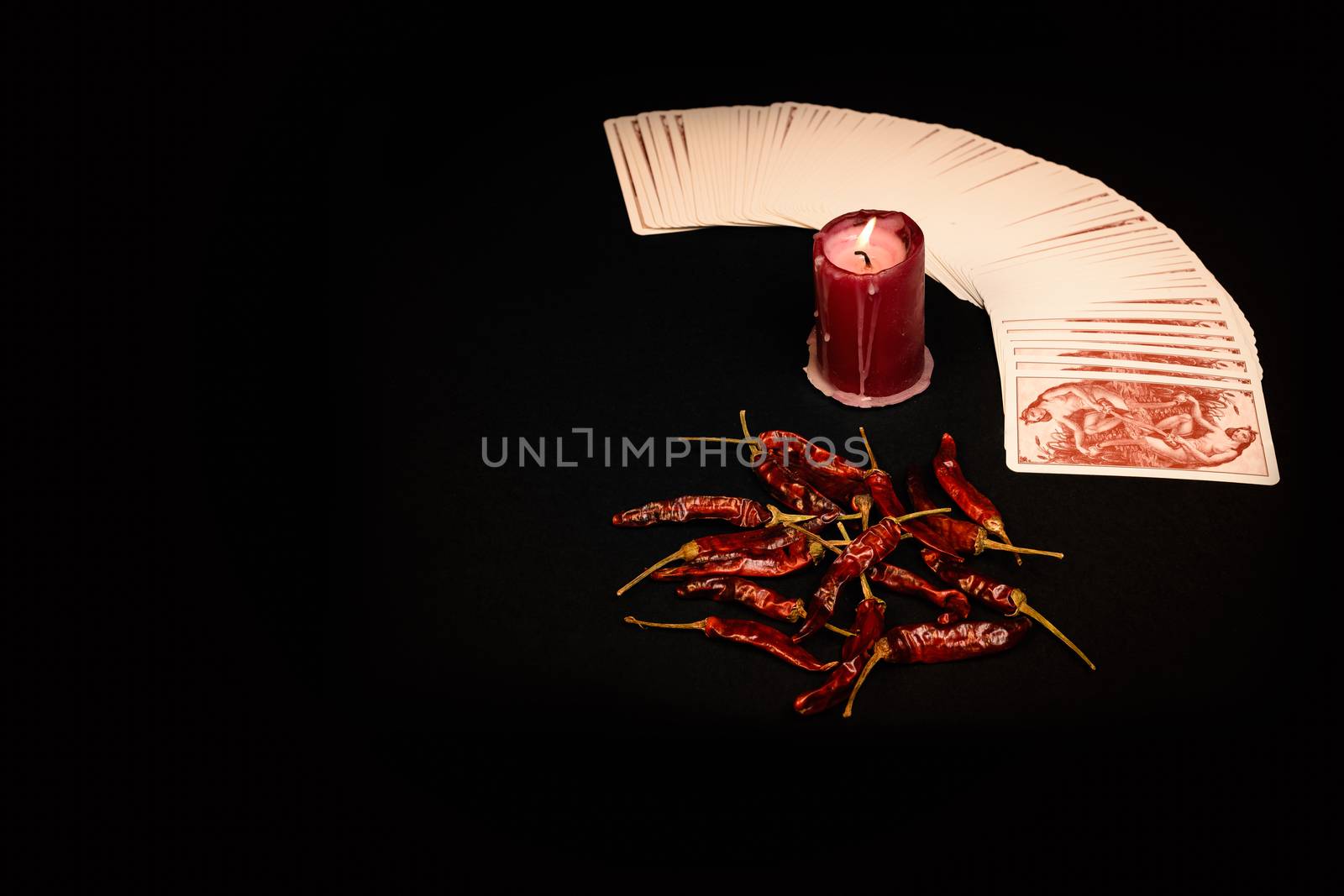 In the pictured a deck of cards open fan , a red candle and red pepper dry.