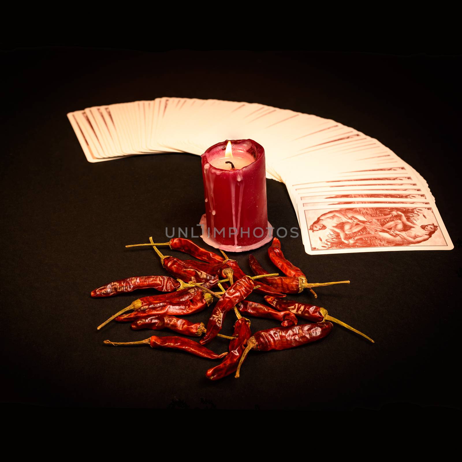 In the pictured a deck of cards open fan , a red candle and red pepper dry.