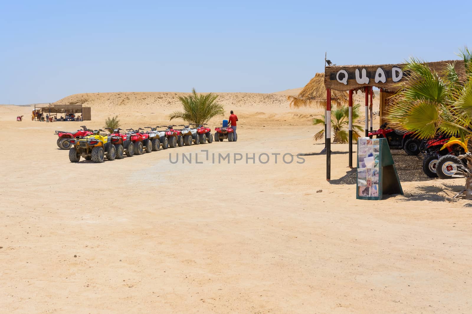 In the picture a row of oblique quad where a man fill up with petrol at the quad and in the background the Egyptian desert