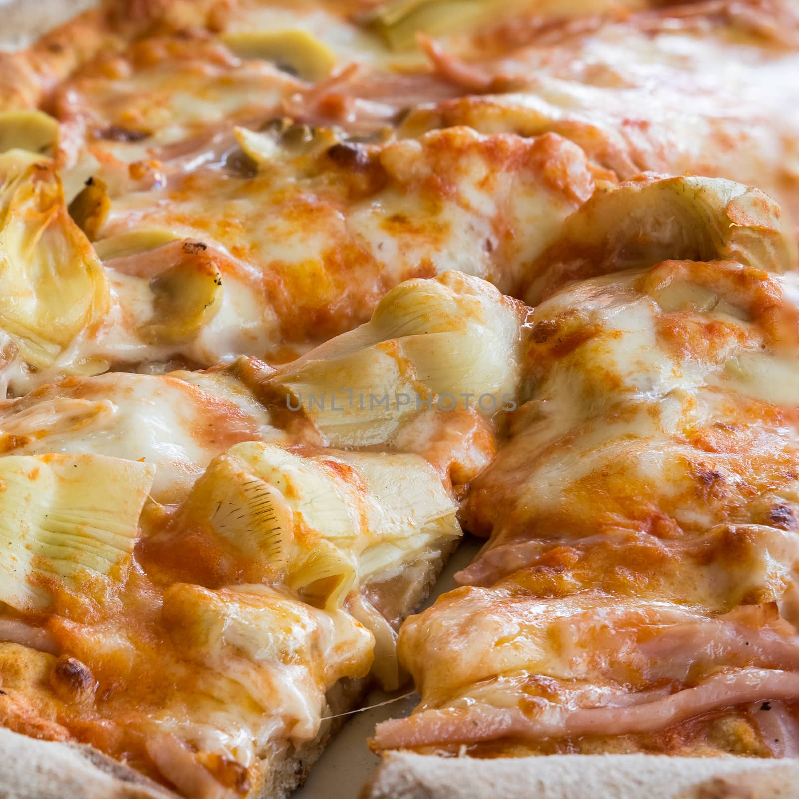 In the picture a cut pizza with tomato, mozzarella, mushrooms, ham and artichokes.
