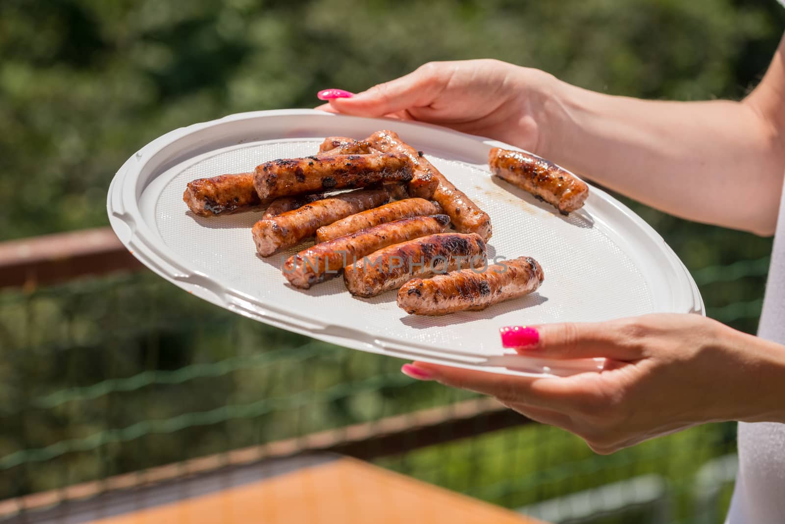 Pictured just cooked pork sausages issued in a plastic plate held by hand.