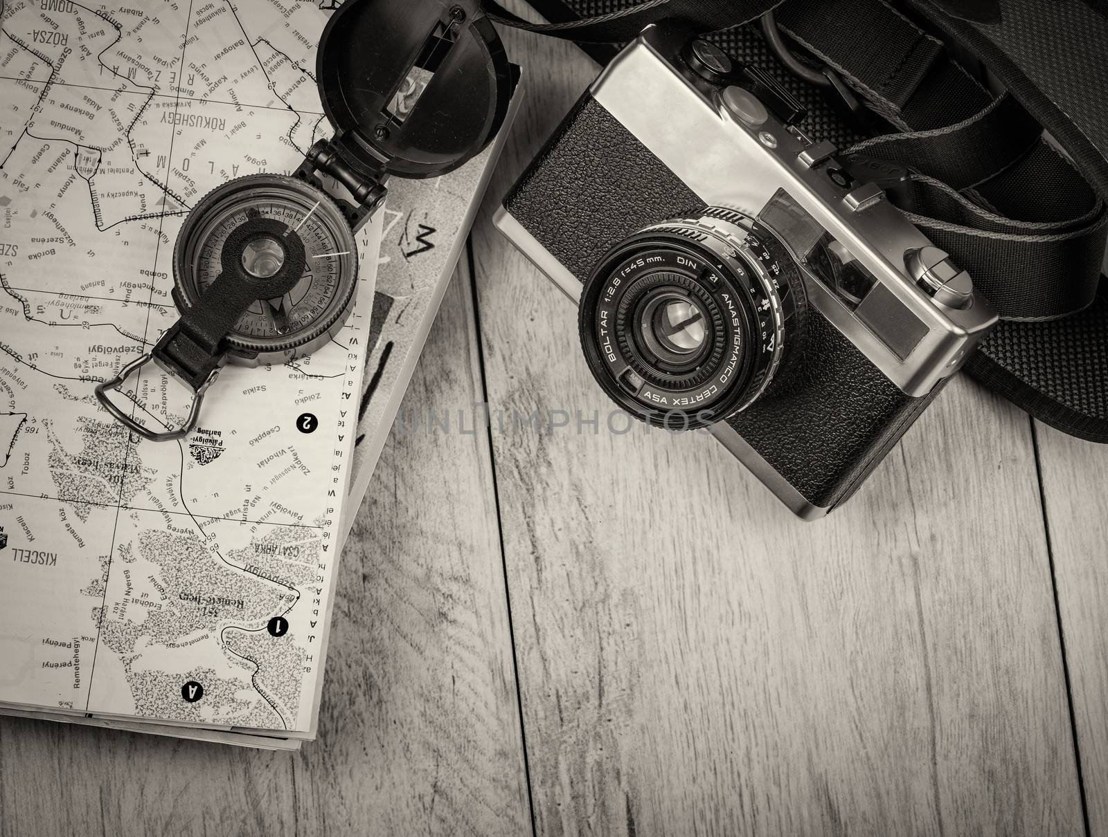 In the picture an analog camera film , a compass,book  and a map, on the sides shells and decorative stones .