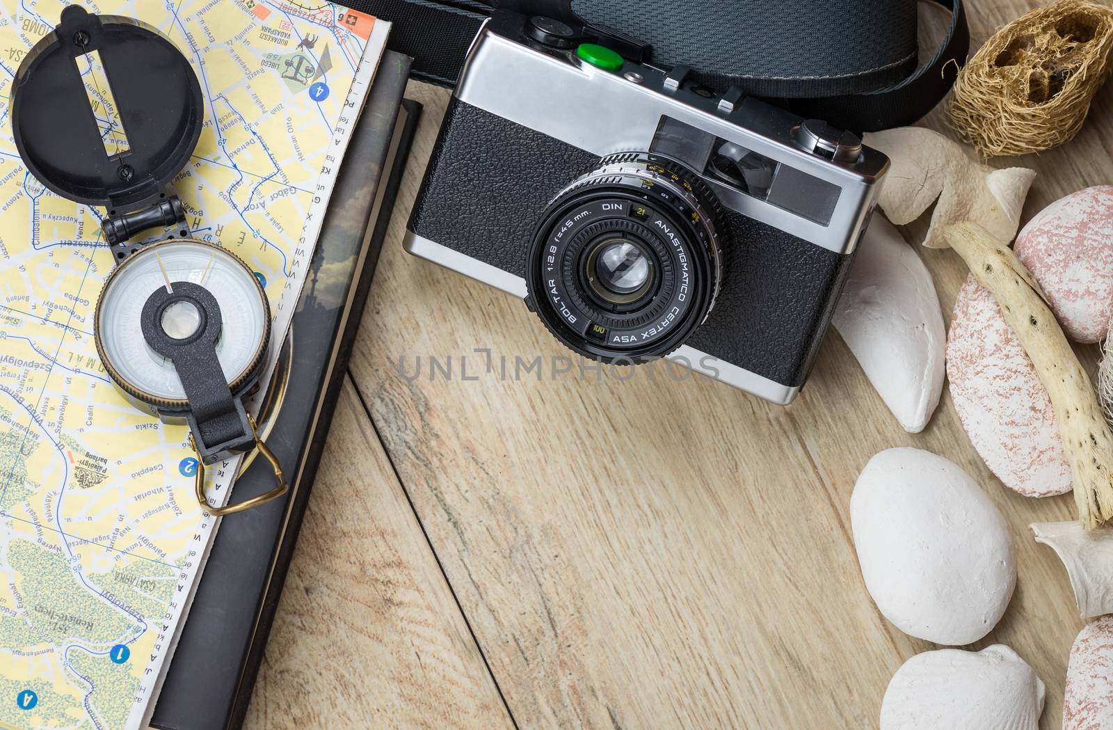 In the picture an analog camera film , a compass,book and a map, on the sides shells and decorative stones .