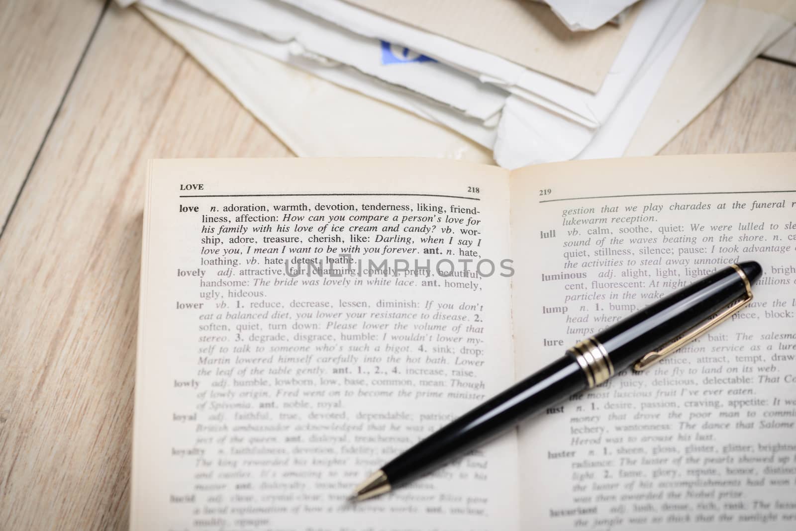 In the picture an open book with pen where the word love is highlighted and its synonyms , the background of the letters .