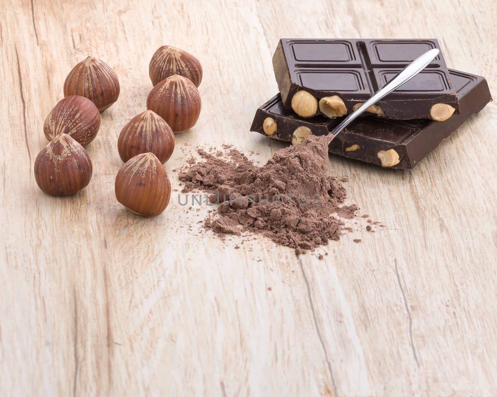 A front view of chocolate, hazelnuts and covered teaspoon cocoa.