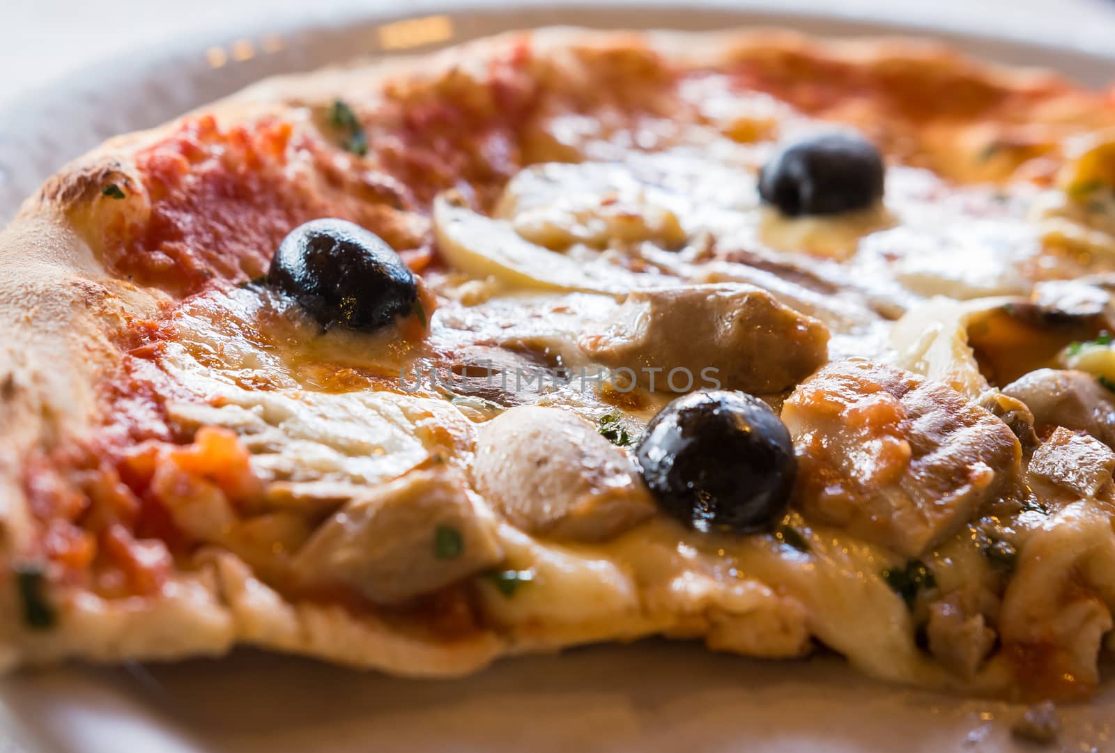 A close-up image of a slice Italian pizza with olives , mushrooms and herbs .