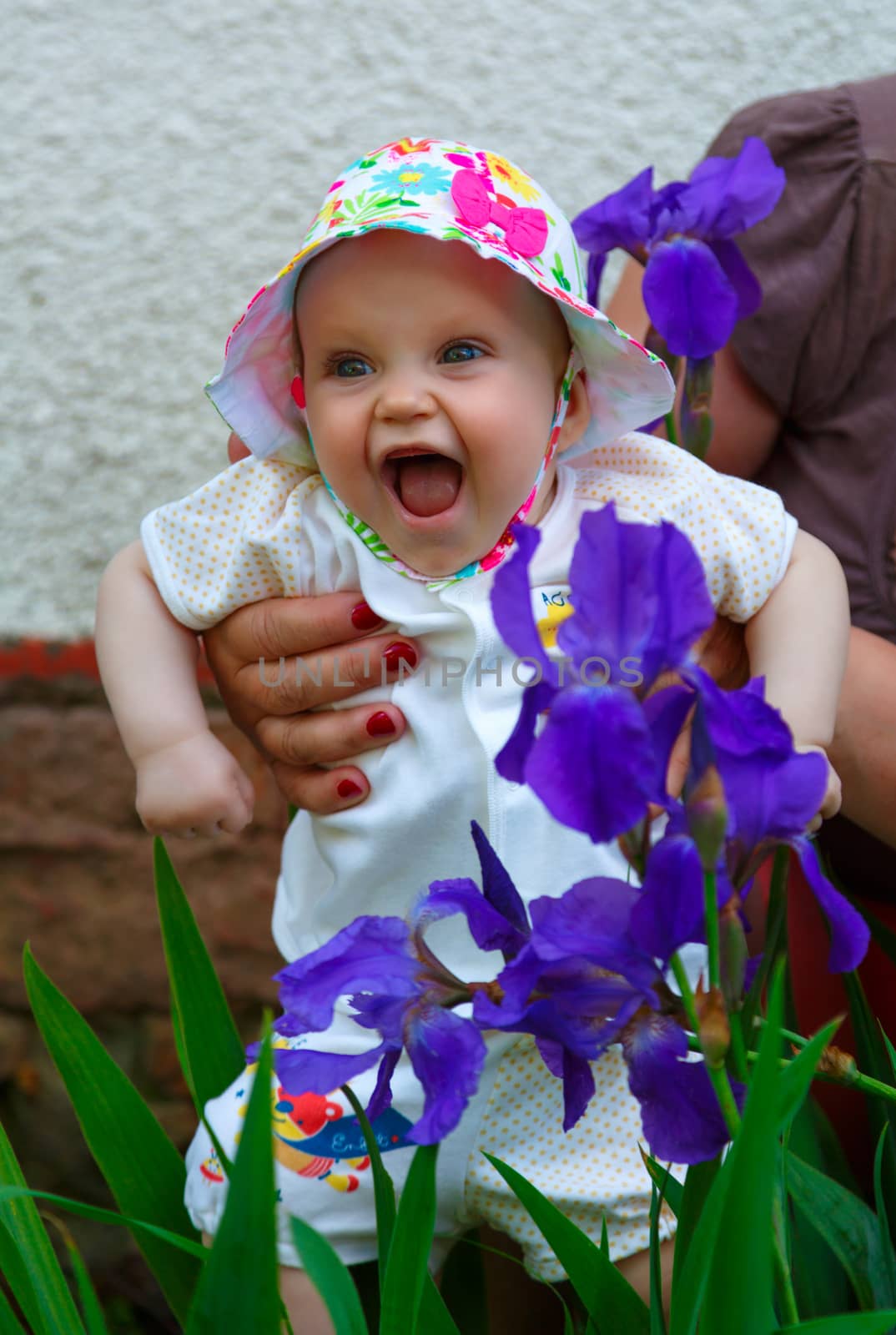 The five-month girl cheerfully laughs, close to the blue irises