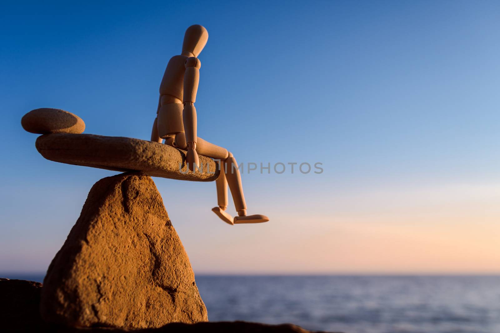 Wooden mannequin sitting on the top of sea stone