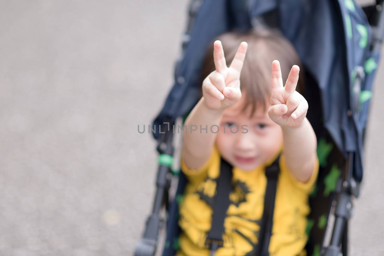 A young boy sitting in a stroller making peace signs with both hands.