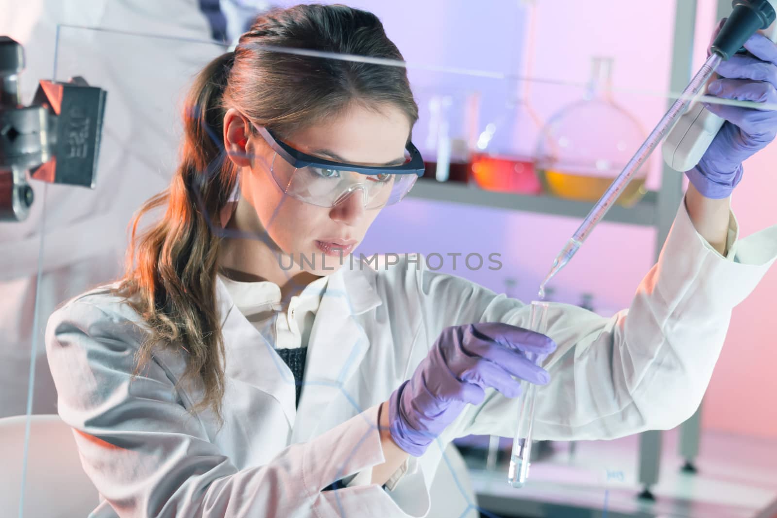 Life scientists researching in laboratory. Focused female life science professional pipetting solution into the glass cuvette. Lens focus on researcher's eyes. Healthcare and biotechnology concept.