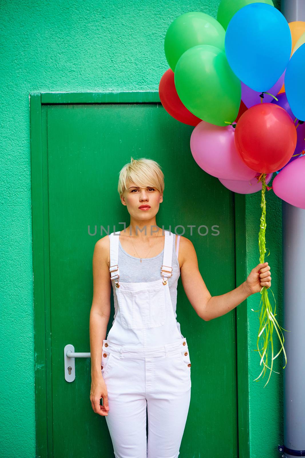 Happy young woman with colorful latex balloons on green background, outdoor