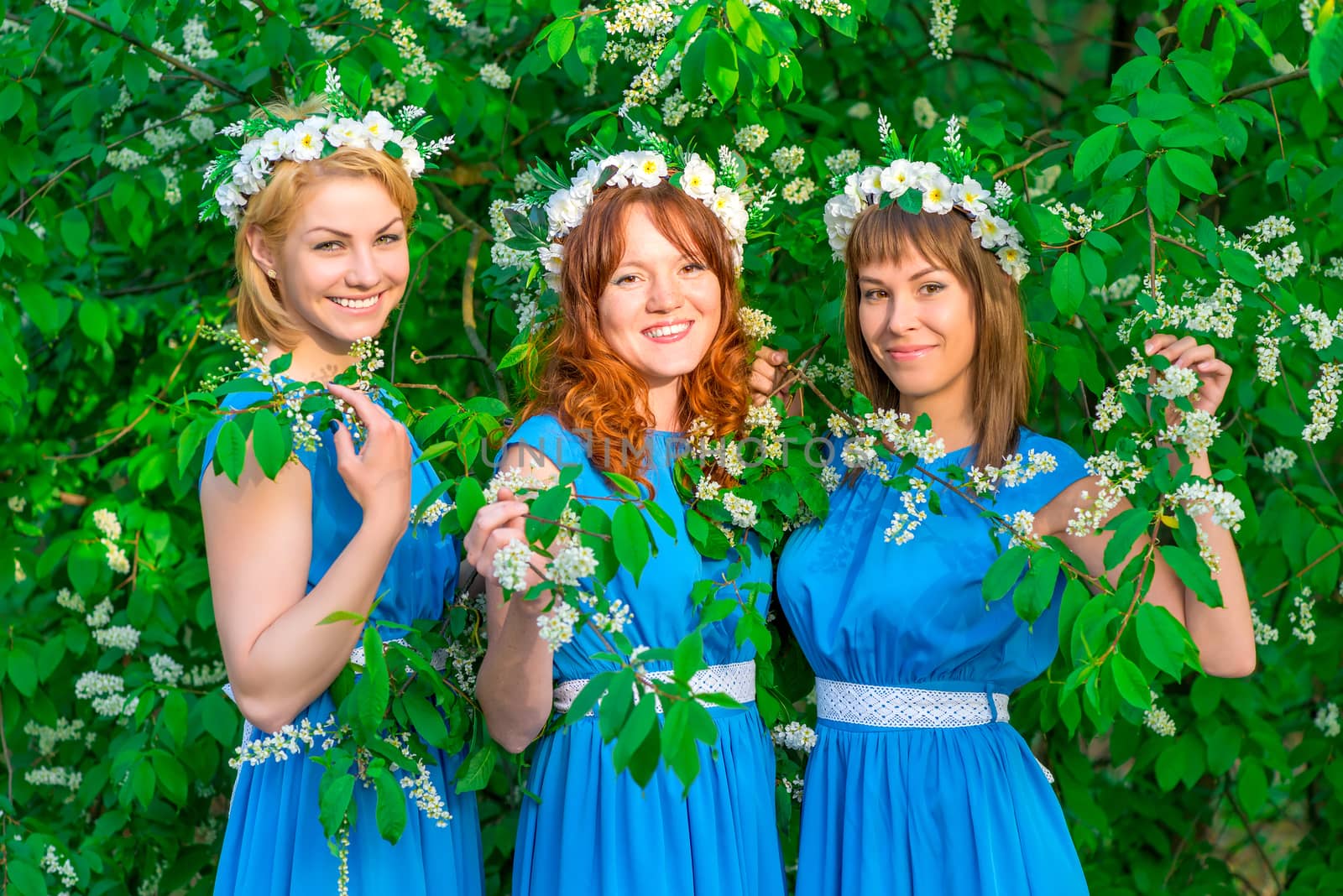 Three happy girls in identical dresses posing in the garden in spring