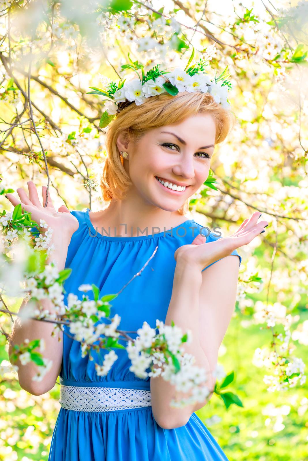 romantic girl with a wreath of flowers on her head near a flowering tree
