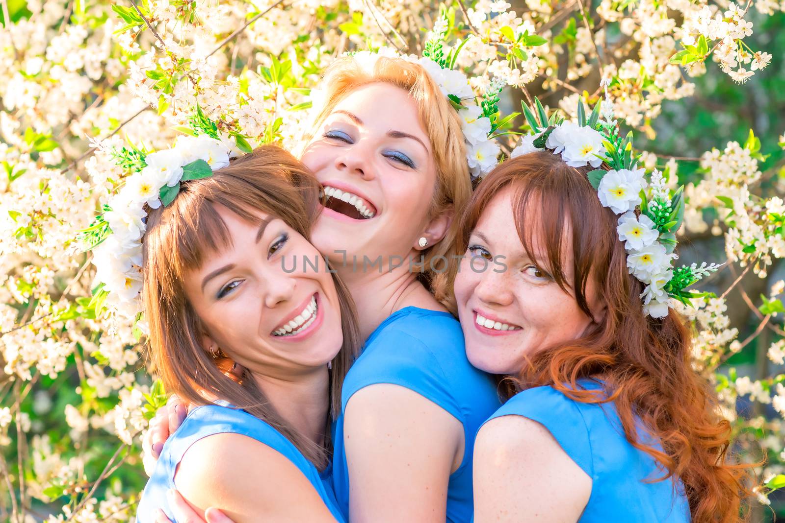 Three laughing girls in blue dresses in the lush spring garden