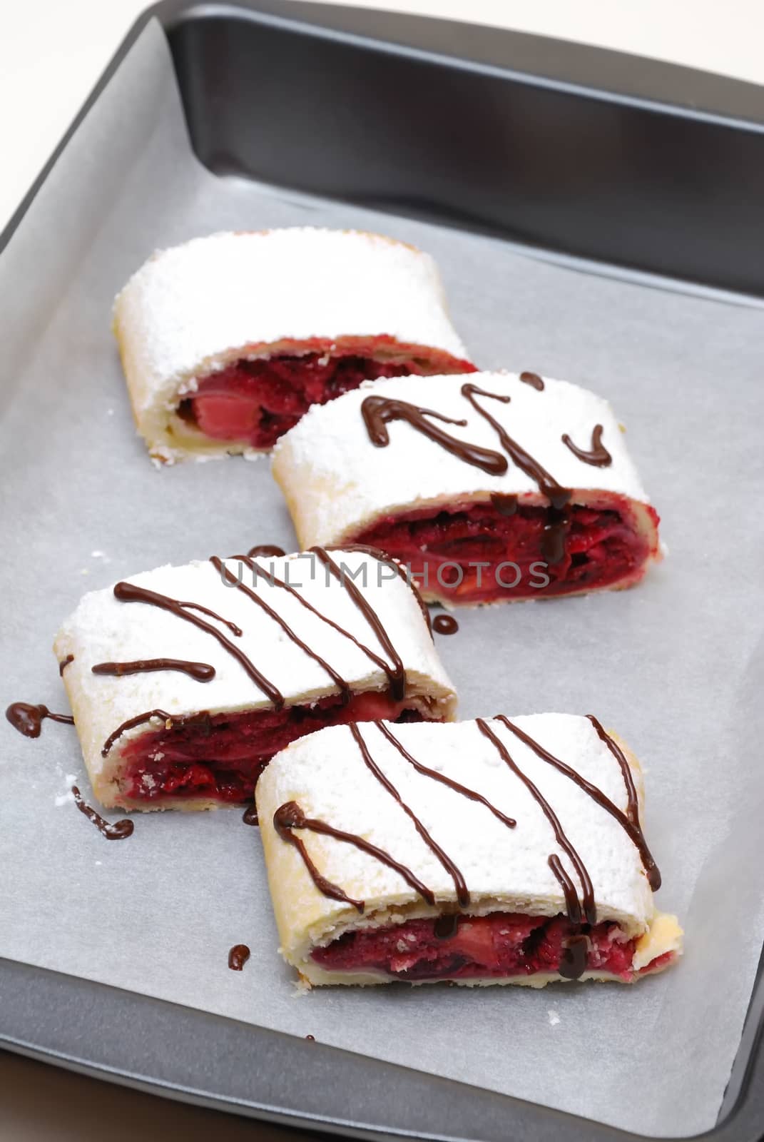 Swiss rolls with cherry and strawberry decorated decorated with chocolate on parchment