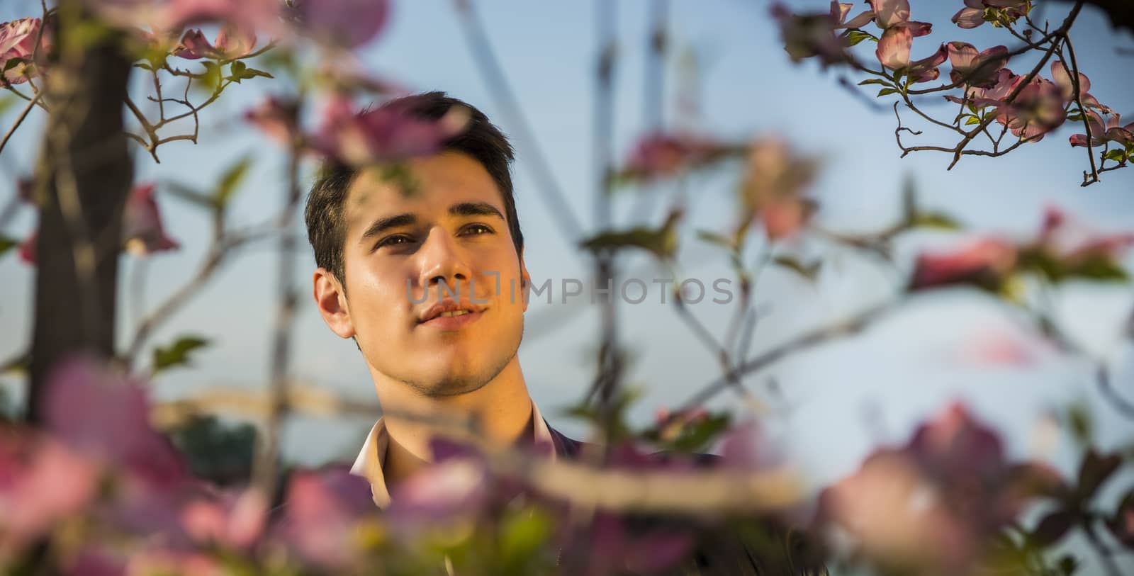 Good looking male model at couuntryside, among flowers, enjoying nature with eyes closed