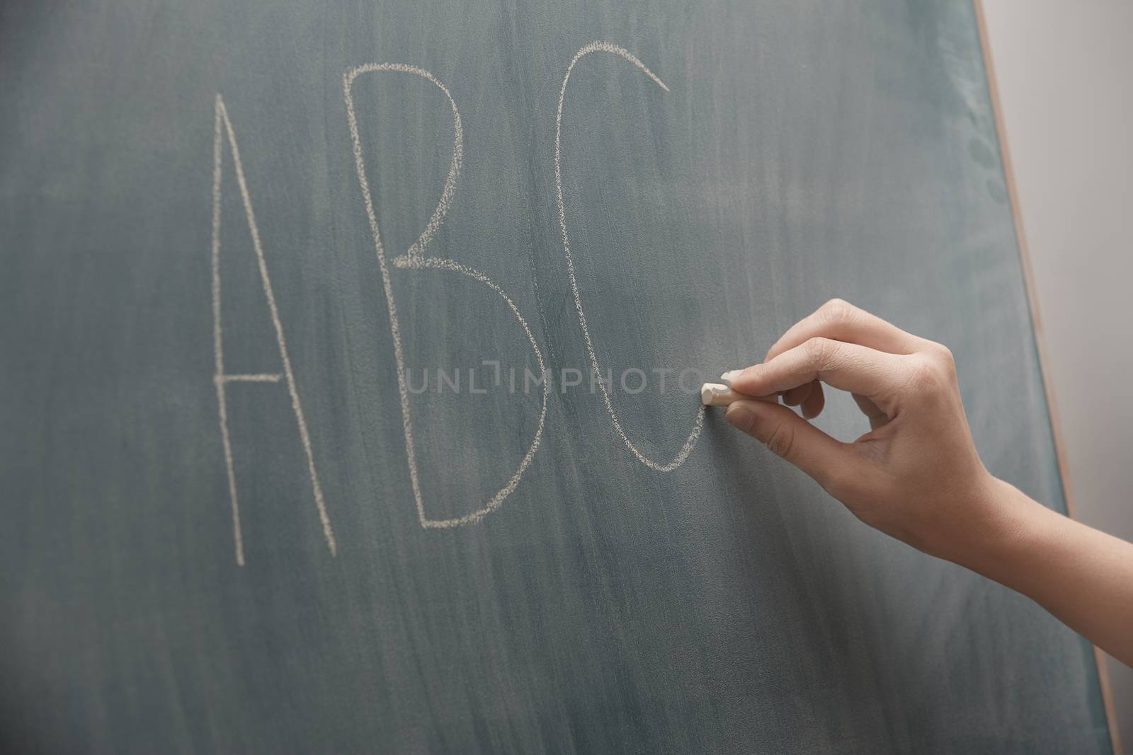 Human hand writing ABC characters on a blackboard