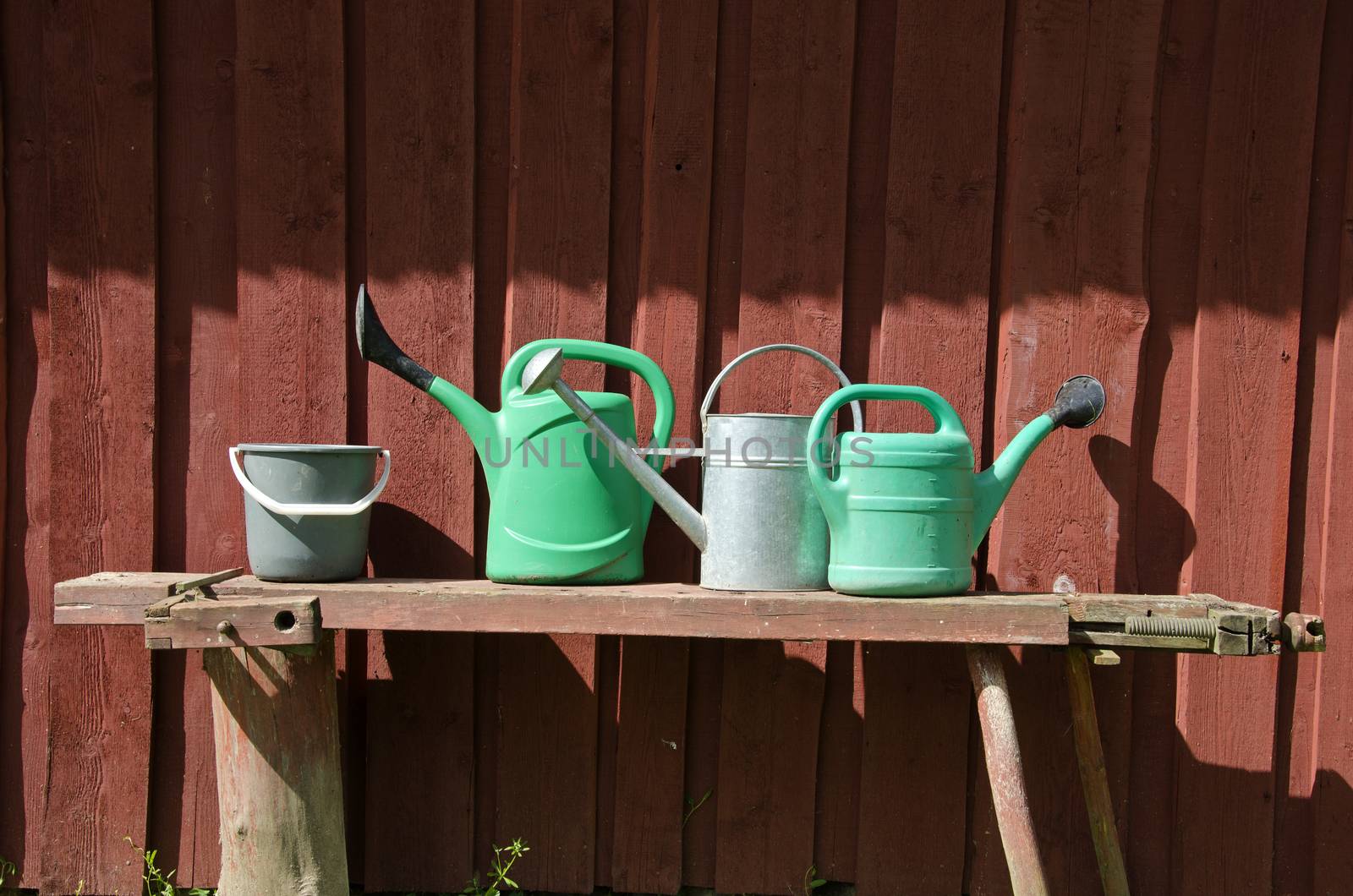 Bucket and three watering pots with red wooden barn wall background