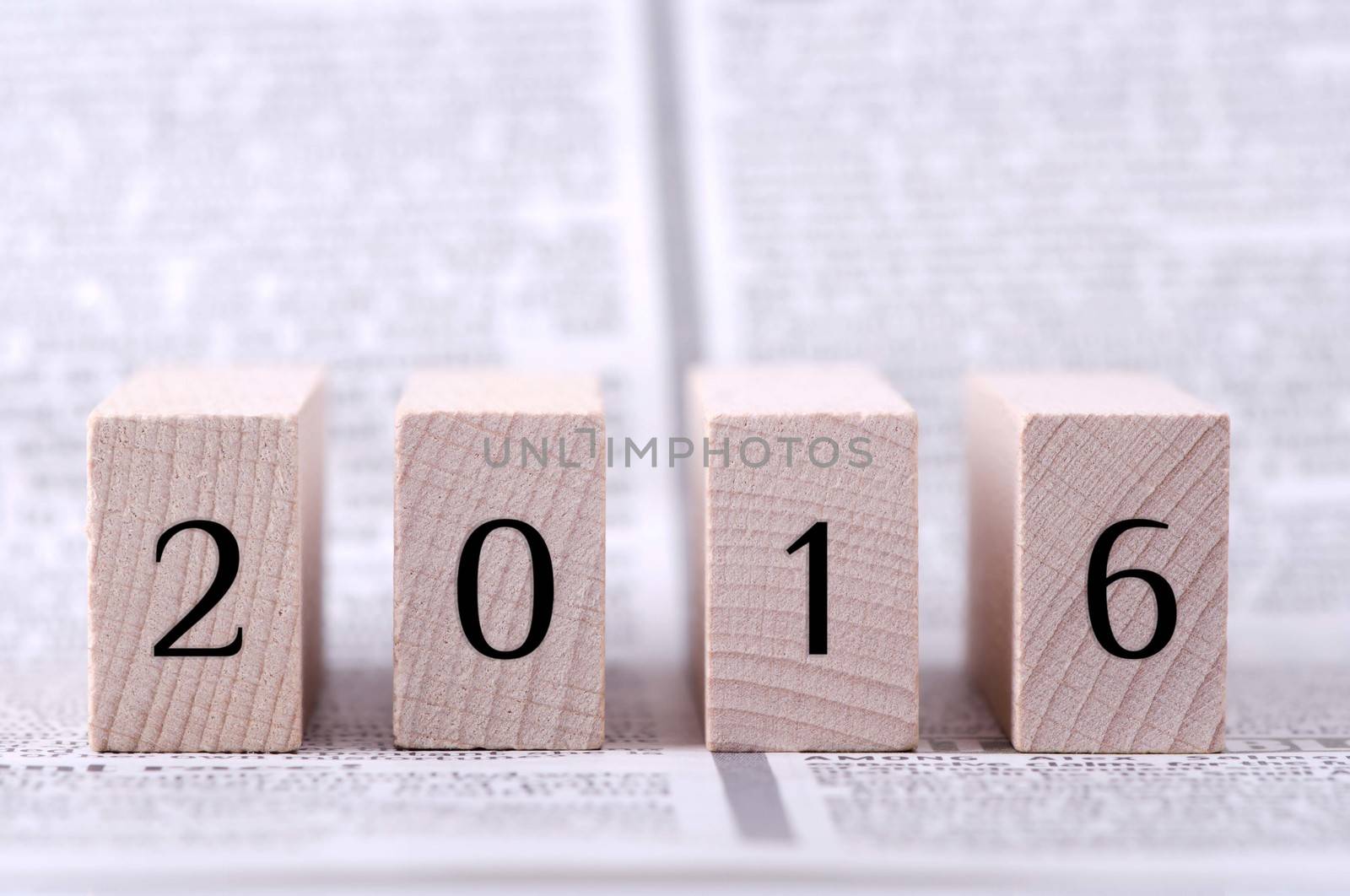 Four wooden blocks with 2016 numerals on newspaper background.