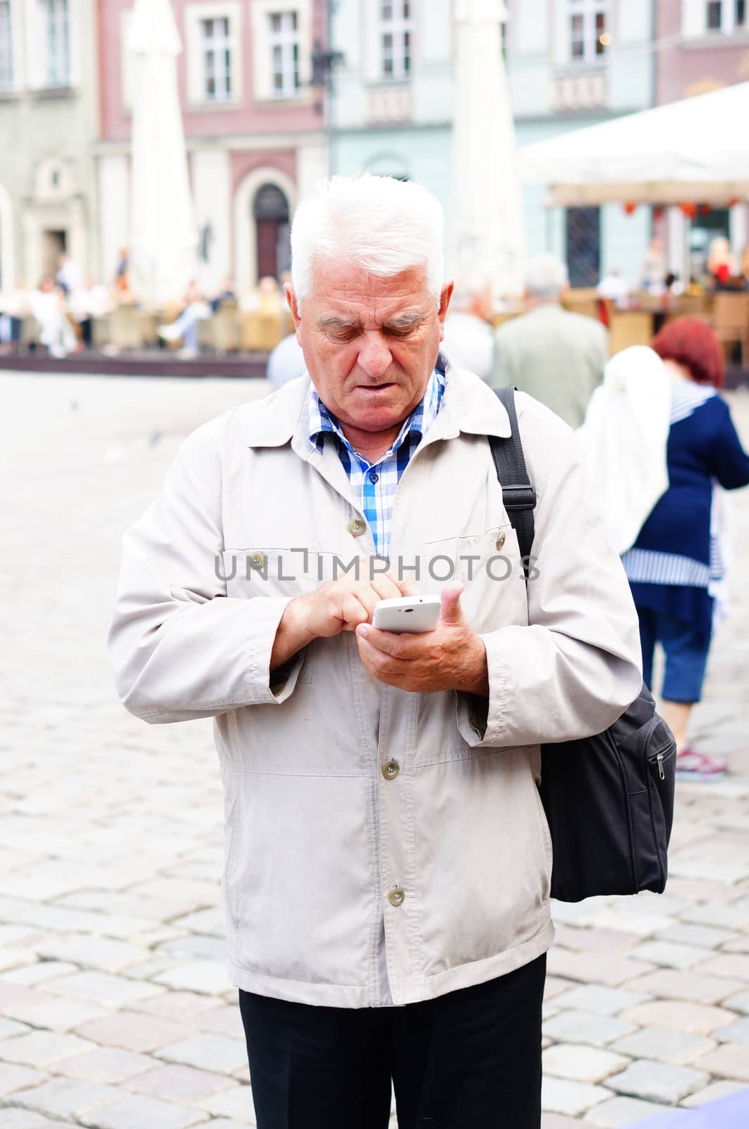 POZNAN, POLAND - SEPTEMBER 13, 2014: Elderly man checking his phone at the old square