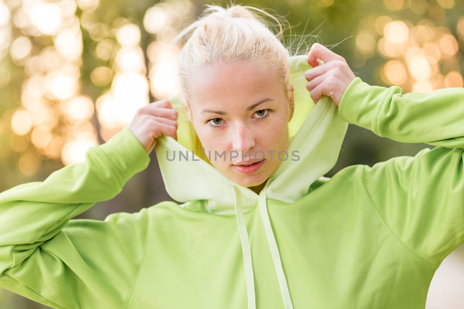 Portrait of attractive confident sporty woman wearing fashionable green hoodie while training in the nature. Active lifestyle and sportswear concept.