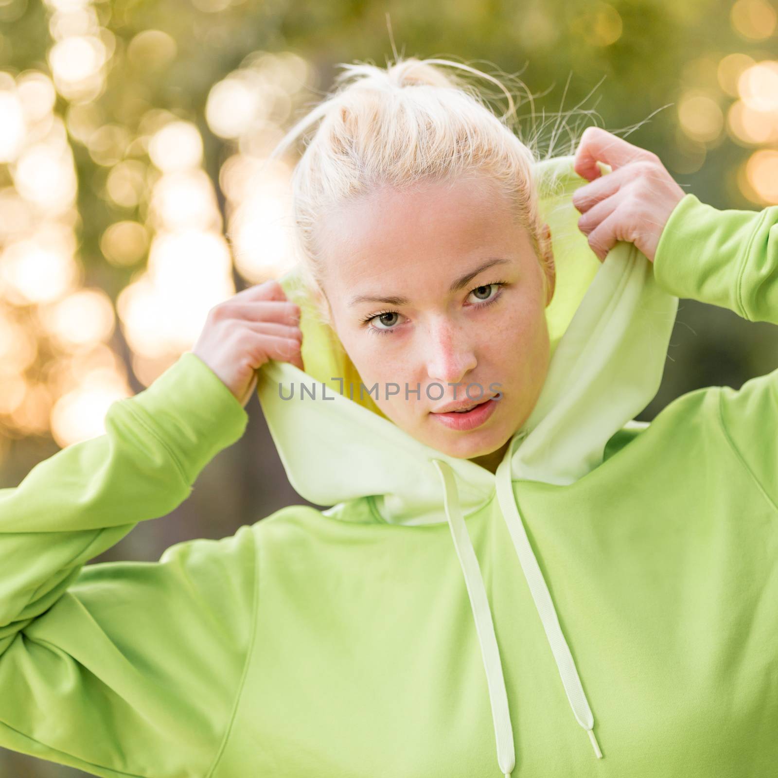 Portrait of attractive confident sporty woman wearing fashionable green hoodie while training in the nature. Active lifestyle and sportswear concept.