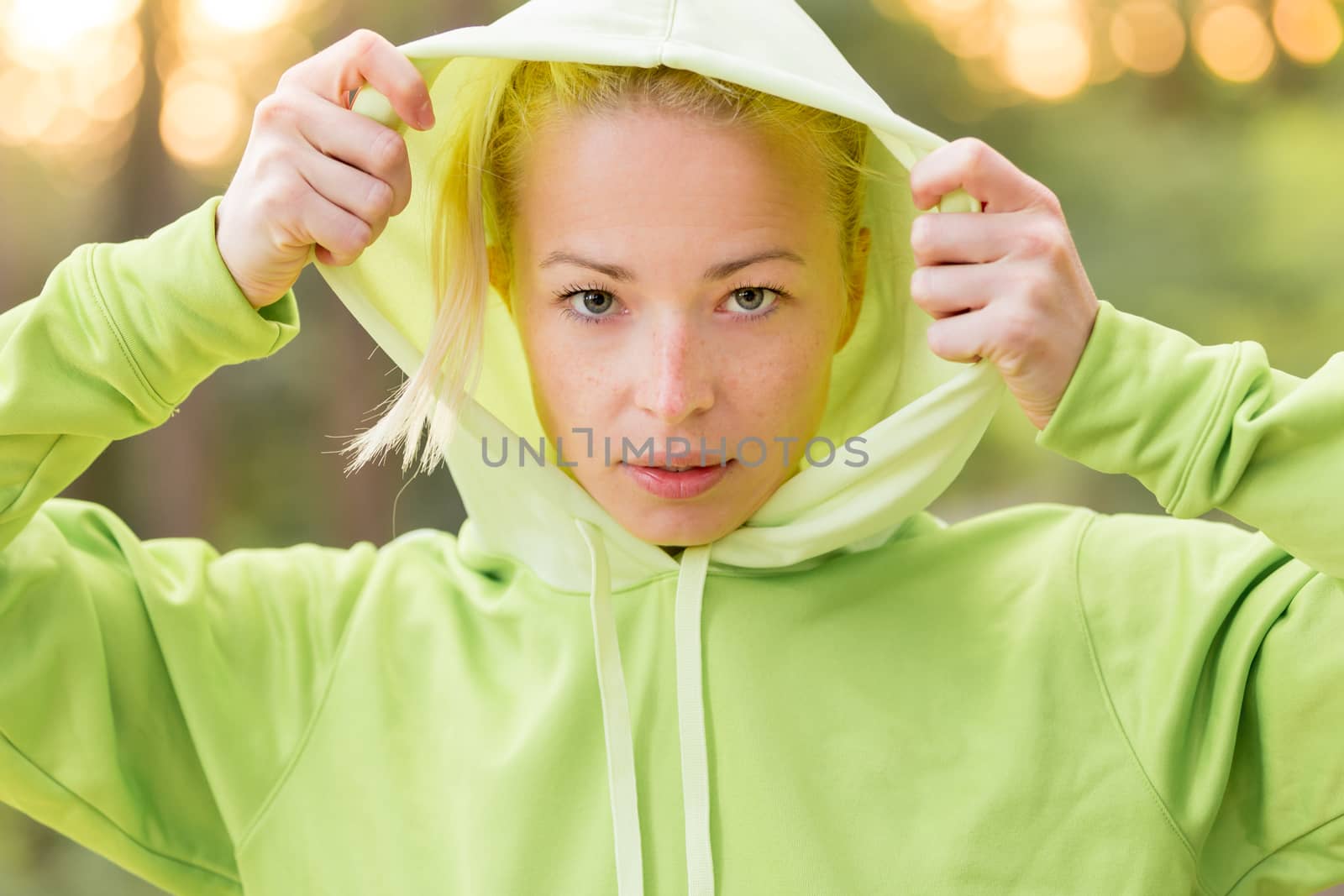 Portrait of attractive confident sporty woman wearing fashionable green hoodie while training in the nature. Active lifestyle and sportswear concept.