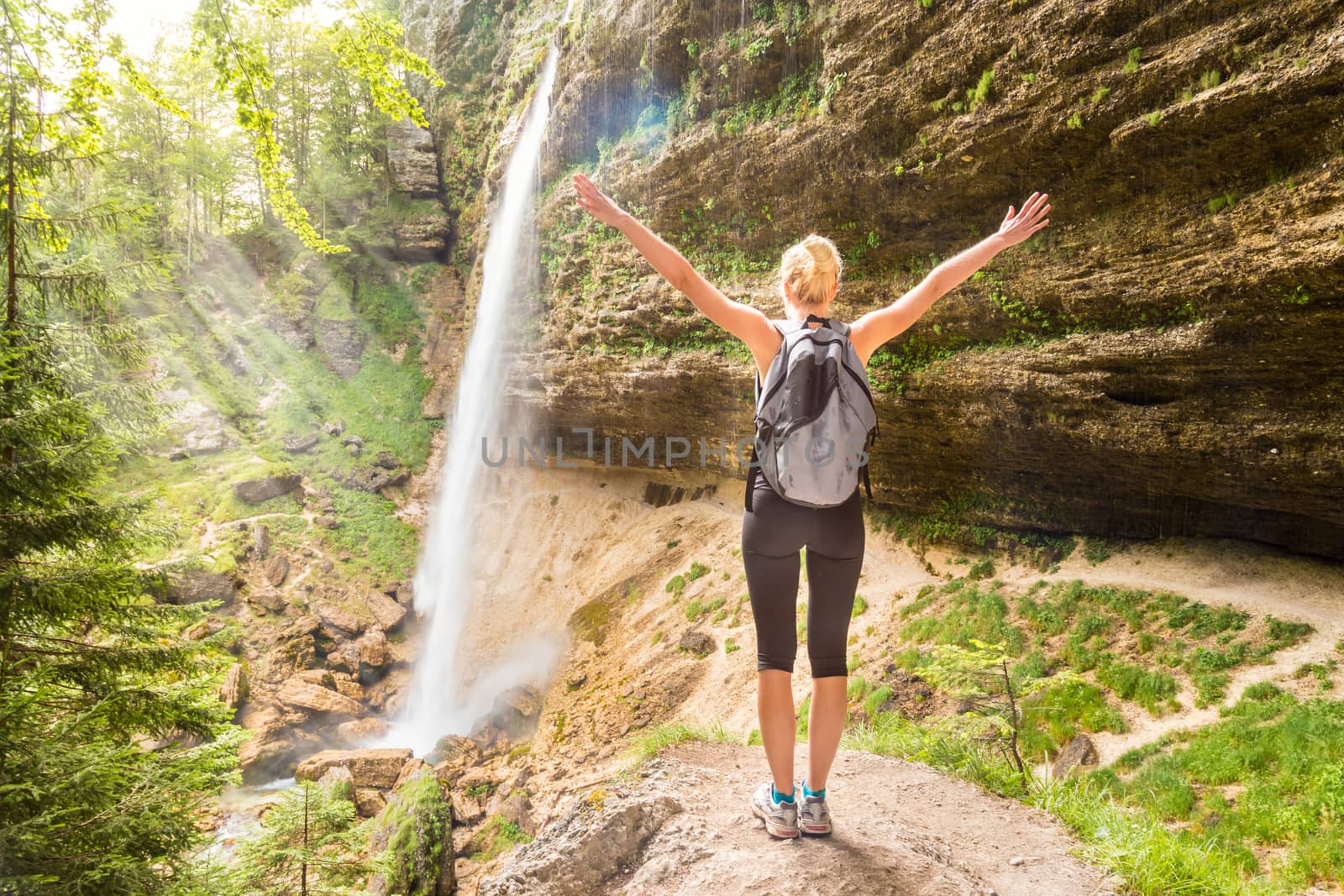 Female hiker raising arms inhaling fresh air, feeling relaxed and free in beautiful natural environment under Pericnik waterfall in Vrata Valley in Triglav National Park in Julian Alps, Slovenia.