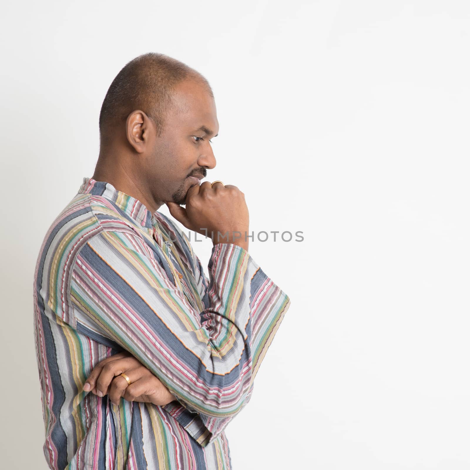 Profile view of mature casual business Indian man thinking, standing on plain background.
