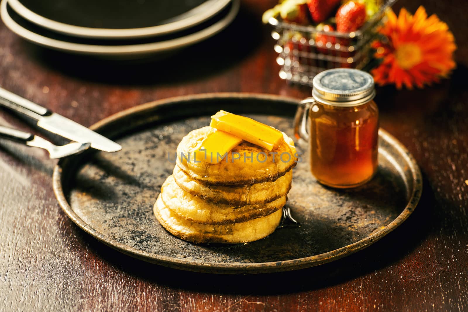 Toasted crumpets with honey drizzled over them and strawberries in the background.