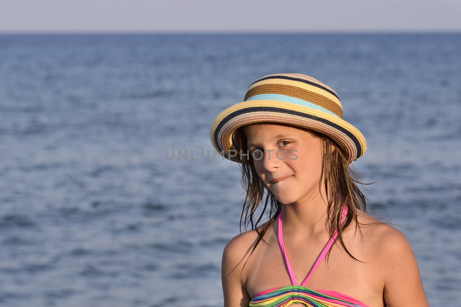 Little girl on the beach at sunset, portrait smiling with a large hat.