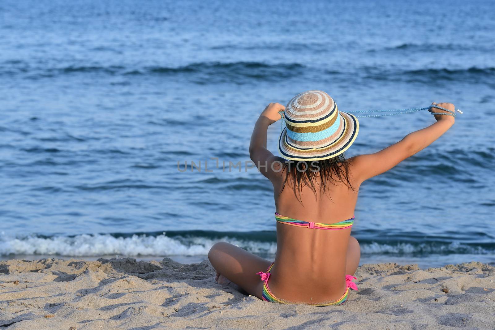 Little girl on the beach at sunset, with her hands she holds a pearls necklace.