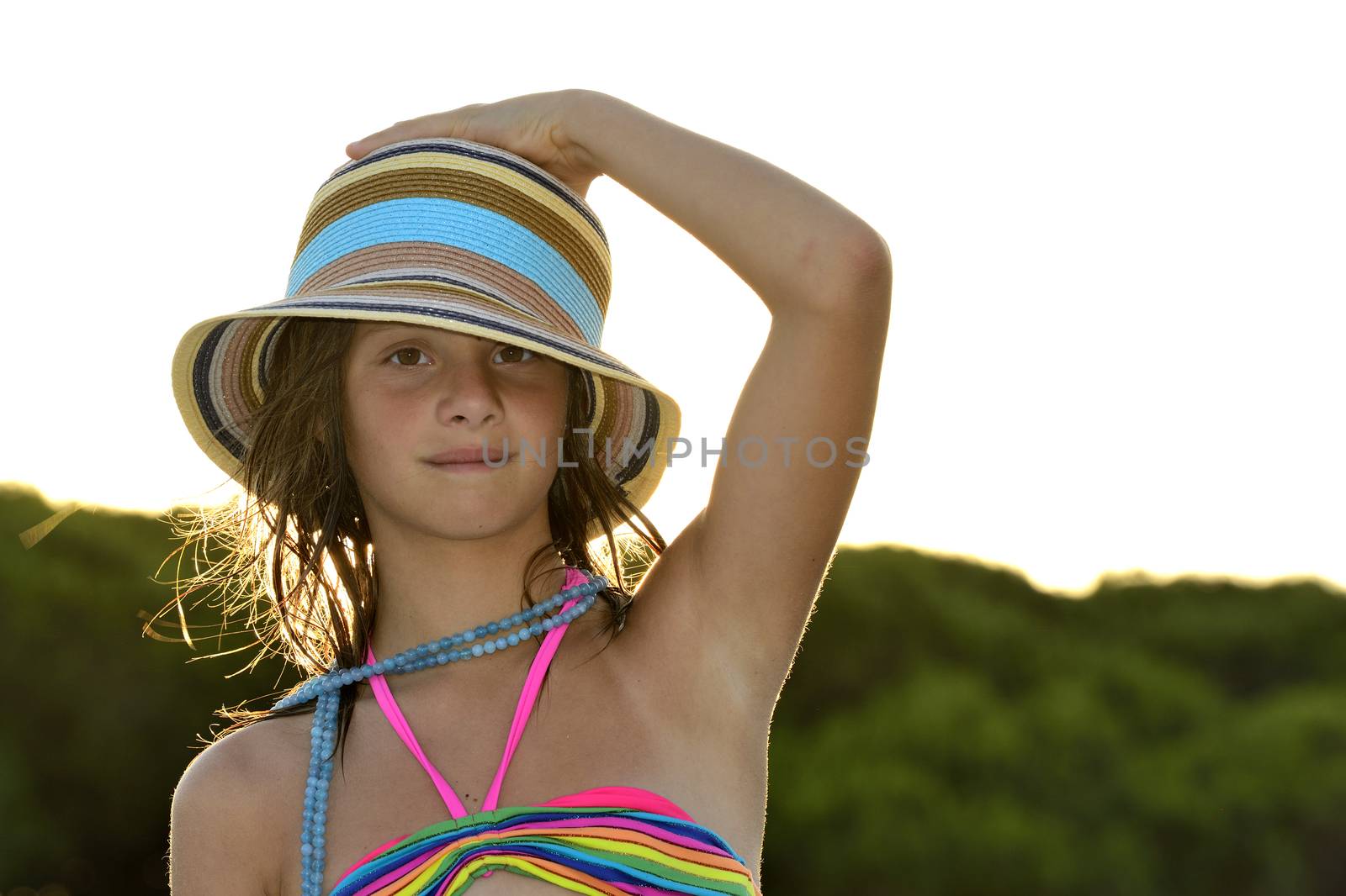 Little girl on the beach at sunset, portrait smiling with a large hat.