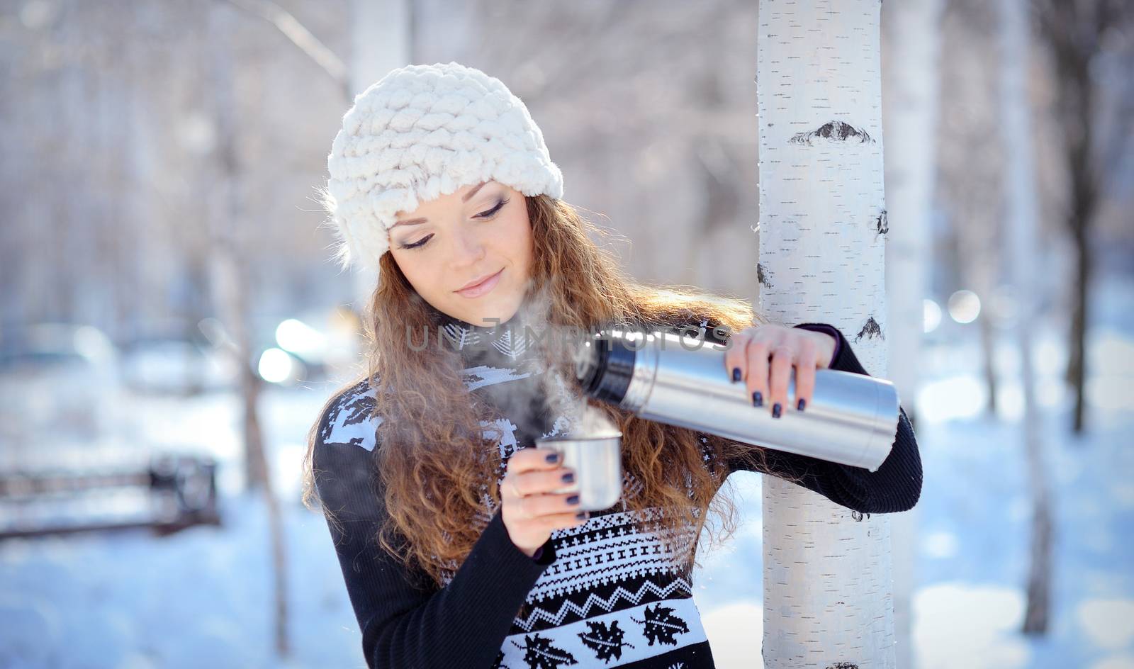 beautiful brunette pours coffee from a thermos for a walk in winter
