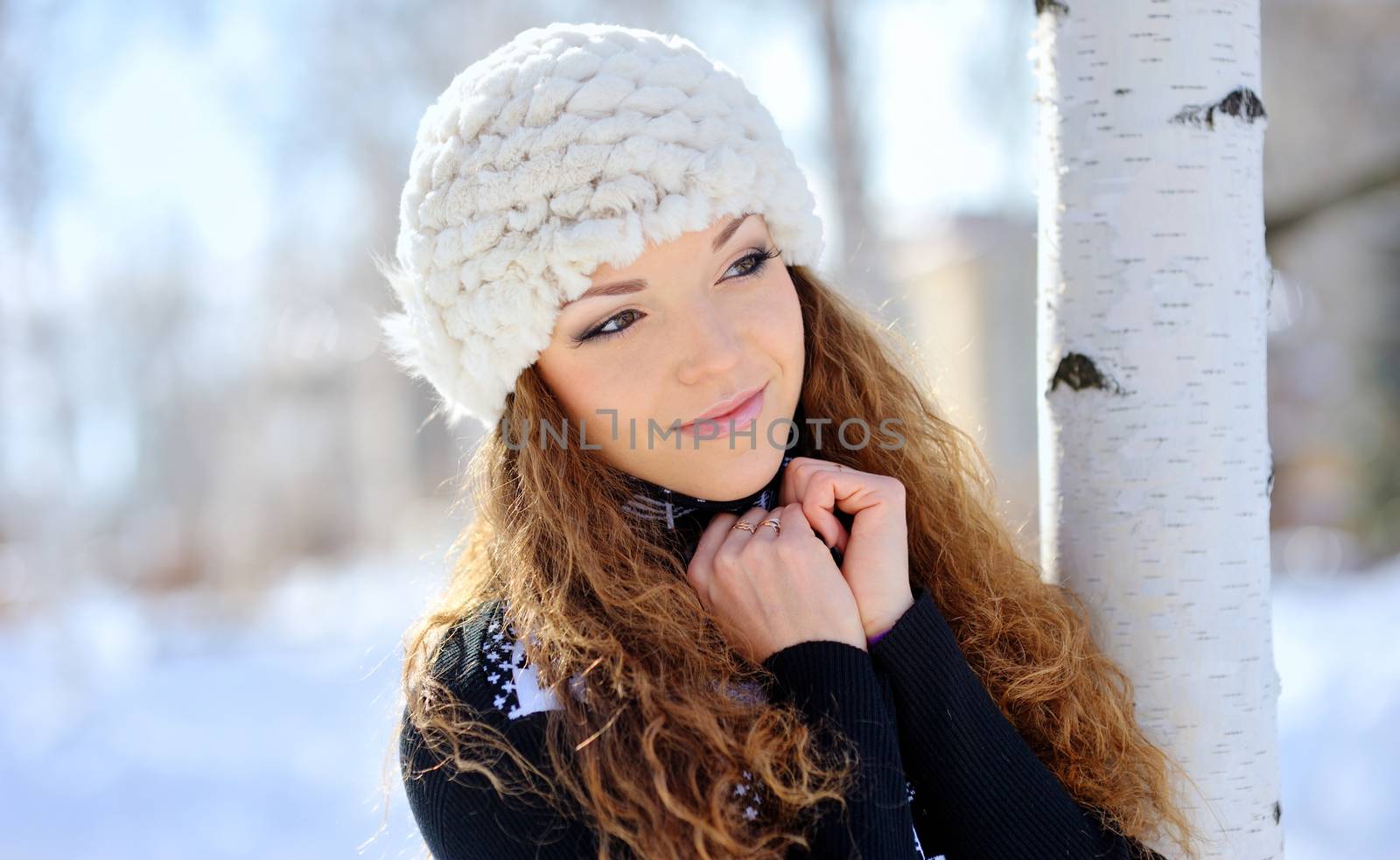 beautiful brunette in a white hat standing near birch in winter