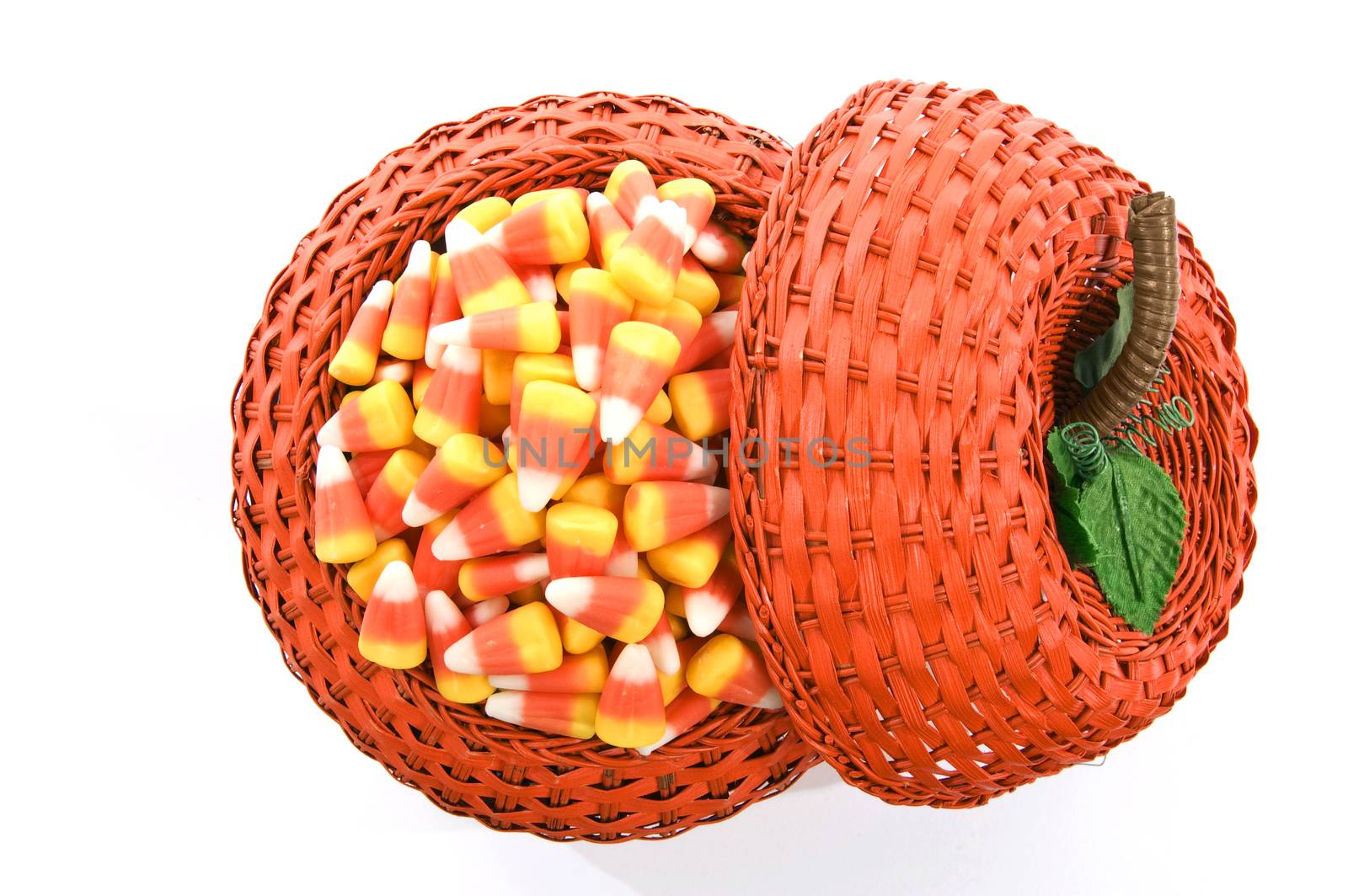 Overhead shot of a cute little wicker pumpkin basket full of candy corn with lid leaning against the pumpkin.