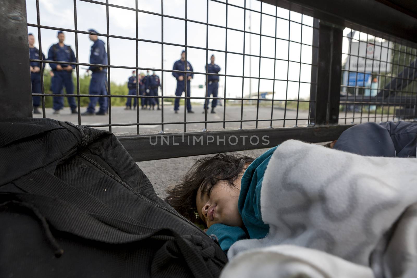 SERBIA, Horgos: A refugee child sleeps behind a border fence as Hungarian border guards appear in the background at the Serbia-Hungary border after Hungary closed the border crossing on September 16, 2015.****Restriction: Photo is not to be sold in Russia or Asia****